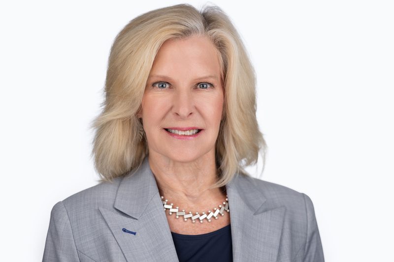 Corporate headshot of a woman in a grey blazer on a white background